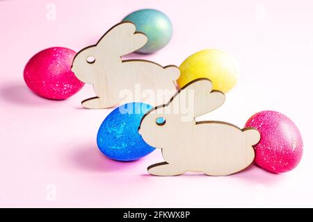Funny wooden Easter Bunny with colorful eggs as symbols of a holiday on light pink background. Stock Photo