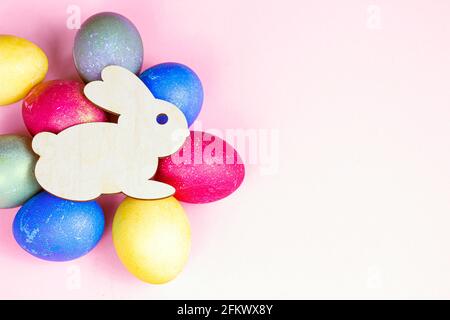 Top view flat lay funny wooden Easter Bunny with colorful eggs as symbols of a holiday with copy space on light pink background. Stock Photo