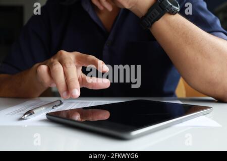 businessman working in the office. he is using touchpad reading an email on tablet and taking notes on the paper with soft-focus and over light in the Stock Photo