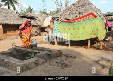 Woman drawing water from a well with rope and container at Kuanarpal village of Cuttack district of Odisha, India Stock Photo