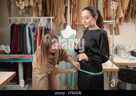 needlewoman tailor taking measures of female client for sew fashion clothes. Stock Photo