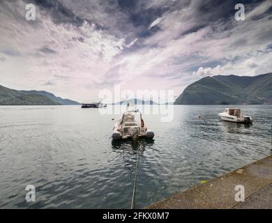 Monte Isola, Italy - April 30, 2021: Moored boats and a ferry on Lake Iseo from Monte Isola, the largest lake island in Europe. Stock Photo