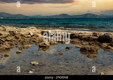 Sunset, sunrise over Mediterranean sea concept. Blue calm sea joins with colorful cloudy sky background. Splashing water creates a pond between the ro Stock Photo