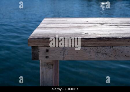 Old empty grey wooden bench, pier over blur blue sea background. Waterfront fish tavern table, wood planks, platform for relaxation, sunny summer day. Stock Photo