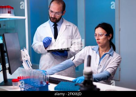 Woman scientist and man doctor studying virus expertise in medicine lab working with professional technology equipment. Doctors specialists discussing innovative treatment using high tech technology equipment for healthcare. Stock Photo