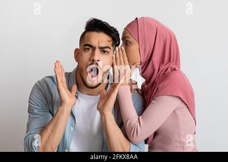 Young woman sharing secret with her shocked black boyfriend, gossiping  together, posing over yellow background Stock Photo - Alamy