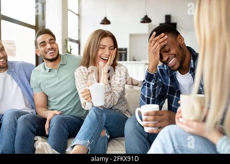 Having fun with friends. Group of young multiracial people drinking coffee at home, joking and laughing together Stock Photo
