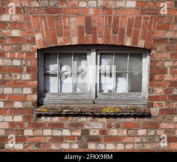 Old Industrial Storage Building, Broken Glass Window Vandalism On An Old Brick Building Boarded up With White Coloured Board Stock Photo