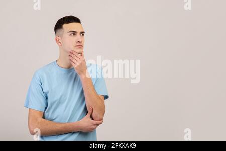 Pensive young guy thinking over problem, making decision, looking at blank space over grey studio background Stock Photo