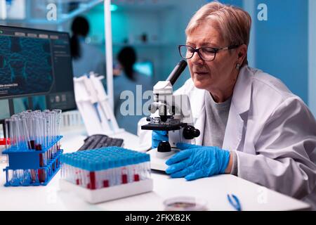 Professional senior scientist using microscope in health study. Laboratory for scientific research with professional equipment for virus study and diagnosis biotechnolog development. Stock Photo