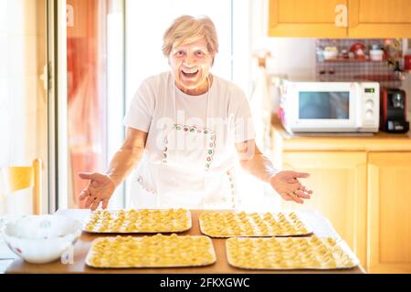 Happy woman presenting handmade ' cappelletti ' at house kitchen - Local food concept with home made italian pasta preparation - Warm bright backlight Stock Photo