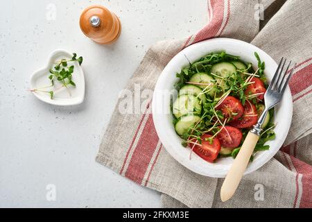 Fresh salad with tomato, cucumber, vegetables, microgreen radishes in white plate on grey stone background. View from above. Concept vegan and healthy Stock Photo