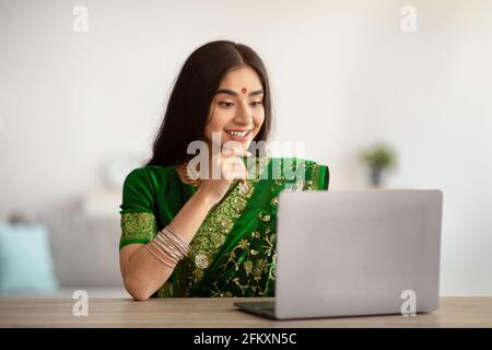 Young Indian lady in beautiful sari dress studying or working online on laptop, indoors Stock Photo