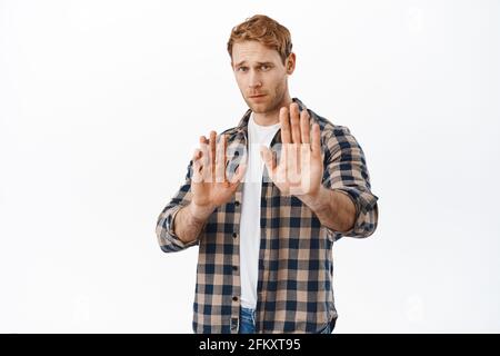 Please stop, stay back. Worried redhead man asking to keep distance, raising hands in prohibit, no gesture, blocking or refusing bad offer, standing Stock Photo