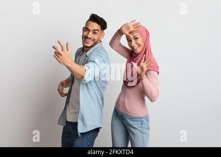 Joyful Muslim Couple Having Fun Together On Grey Background, Dancing And Laughing Stock Photo