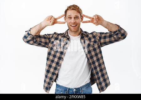 Funny handsome adult man dancing, showing peace v-sign and smiling, stay positive, cheer you up, fool around and showing fun faces, standing over Stock Photo