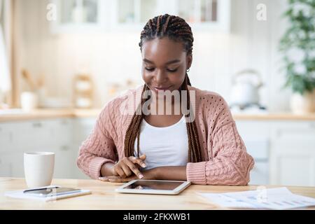 Portrait Of Smiling Young Black Female Relaxing With Digital Tablet In Kitchen, Stock Photo