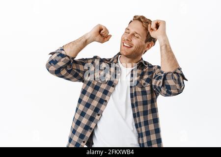 Image of handsome adult redhead man dancing with closed eyes, happy face and smile, relaxing on dance floor, enjoying music, standing against white Stock Photo