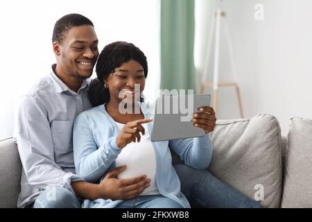 Loving pregnant black couple using digital tablet at home Stock Photo