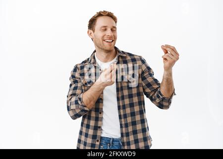 Image of joyful redhead man snap fingers to rhythm of music, dancing with close eyes and satisfied face expression, enjoying party, celebrating Stock Photo