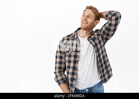 Image of handsome and confident macho man with red hair and strong arms, holding hands behind head, looking aside and smiling satisfied, resting Stock Photo