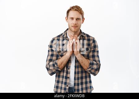 Image of thoughtful redhead man steeple fingers and looking at camera pensive, thinking about something, have a plan, standing against white Stock Photo