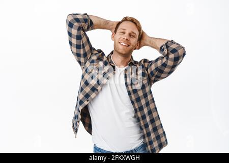 Image of handsome redhead man holding hands behind head and smiling pleased, feeling relaxed and confident, making charming smile, flirty face Stock Photo