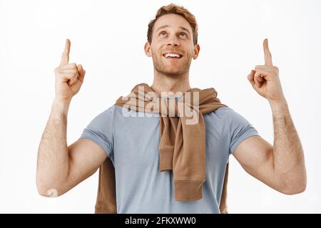 Image of handsome redhead man looking and pointing fingers up with dreamy happy face, checking out something cool, staring at promo deal above Stock Photo