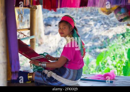 A young Karen  long neck tribe girl weaves silk on her loom in a  Karen Village of Northern Thailand.  ( often referred to as Padaung  people) Stock Photo