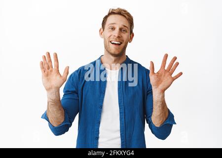 Bye hello. Smiling handsome young man waving hands and looking friendly, say farewell goodbye or hi, greeting someone, standing over white background Stock Photo