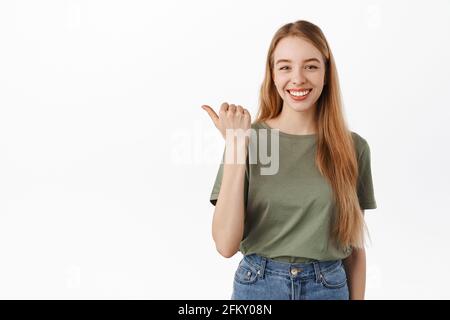 Your logo here. Smiling confident girl student pointing thumb left and looking determined, give advice, recommend this product, showing advertisement Stock Photo