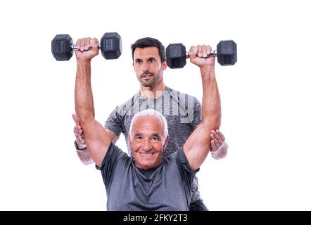 Elderly male client exercising with a fitness trainer, lifts dumbbells. On a white isolated background. Stock Photo