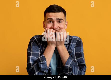 Young Caucasian man feeling scared, biting his nails in panic on orange studio background. Negative human emotions Stock Photo