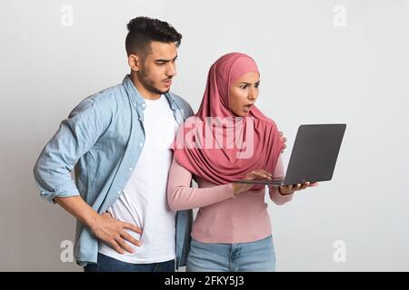 Internet Scams. Confused Young Muslim Couple Looking At Laptop Screen With Worry Stock Photo