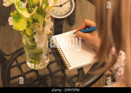Woman writes on notebook over shoulder view, cozy workspace photo concept with glass table Stock Photo