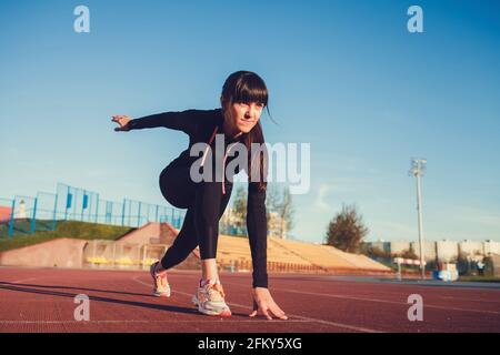 Sportswoman in starting position ready for running. Female athlete about to start a sprint on stadium Stock Photo