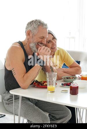 Happy mature husband and older wife having fun eating breakfast at home. Stock Photo