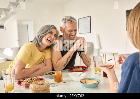 Happy mature family couple having breakfast with daughter sit at kitchen table. Stock Photo