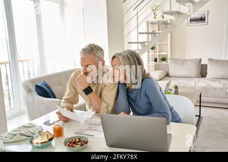 Worried old senior couple checking bank documents or bills at home. Stock Photo