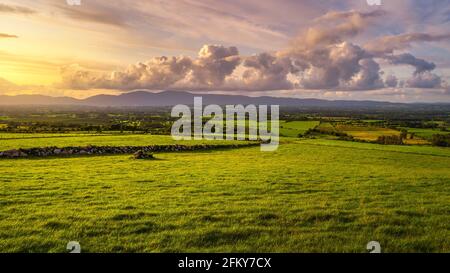 Beautiful sunset with dramatic sky at golden hour over green fields and farms in MacGillycuddys Reeks mountains, Ring of Kerry, Ireland Stock Photo
