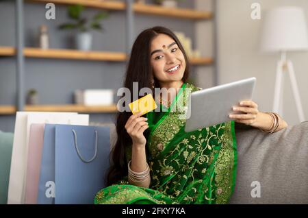 Attractive Indian woman in ethnic sari dress using credit card and tablet computer for online shopping at home Stock Photo
