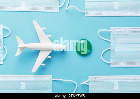A white plane surrounded by protective masks on a blue background with a green and red dot as the destination. The concept of allowing and banning air Stock Photo