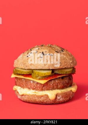 Homemade vegan burger with soy patty, cashew cheese and vegan sauces. Plant-based burger isolated on a red-colored background. Stock Photo