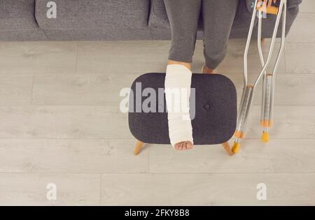 Female broken injured leg relaxing on stool in cast and metal crutches Stock Photo