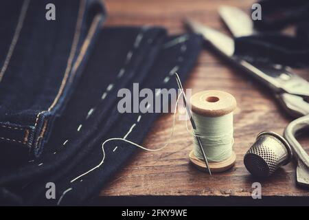 Shortening jeans. Wooden spool of  thread, thimble and scissors on table. Jeans cutting. Stock Photo