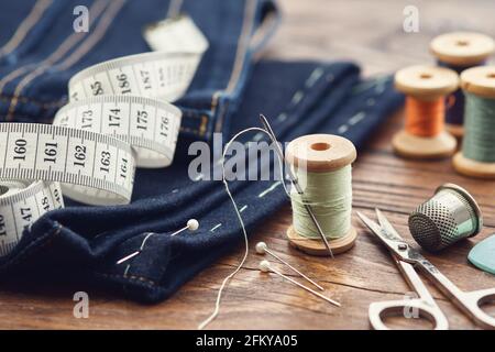 Shortening jeans. Measuring tape, scissors, spools of thread, thimble, including pins and chalk on table. Jeans cutting. Stock Photo