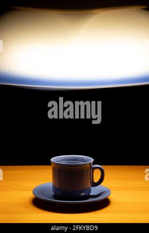 A teacup on the table under a light of moving chandelier, on a black background Stock Photo