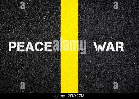 Antonym concept of PEACE versus WAR, written on dark wet asphalt. Top view. Yellow road marking line between the words. Viewed from above. Stock Photo