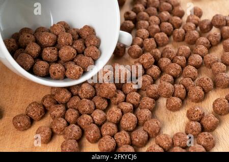 Chocolate cereal balls are scattered over the board with a white teacup. Round flakes. Close-up Stock Photo