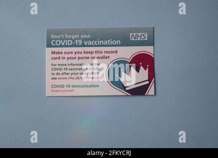 Covid-19 NHS vaccination card on blue background. Stock Photo